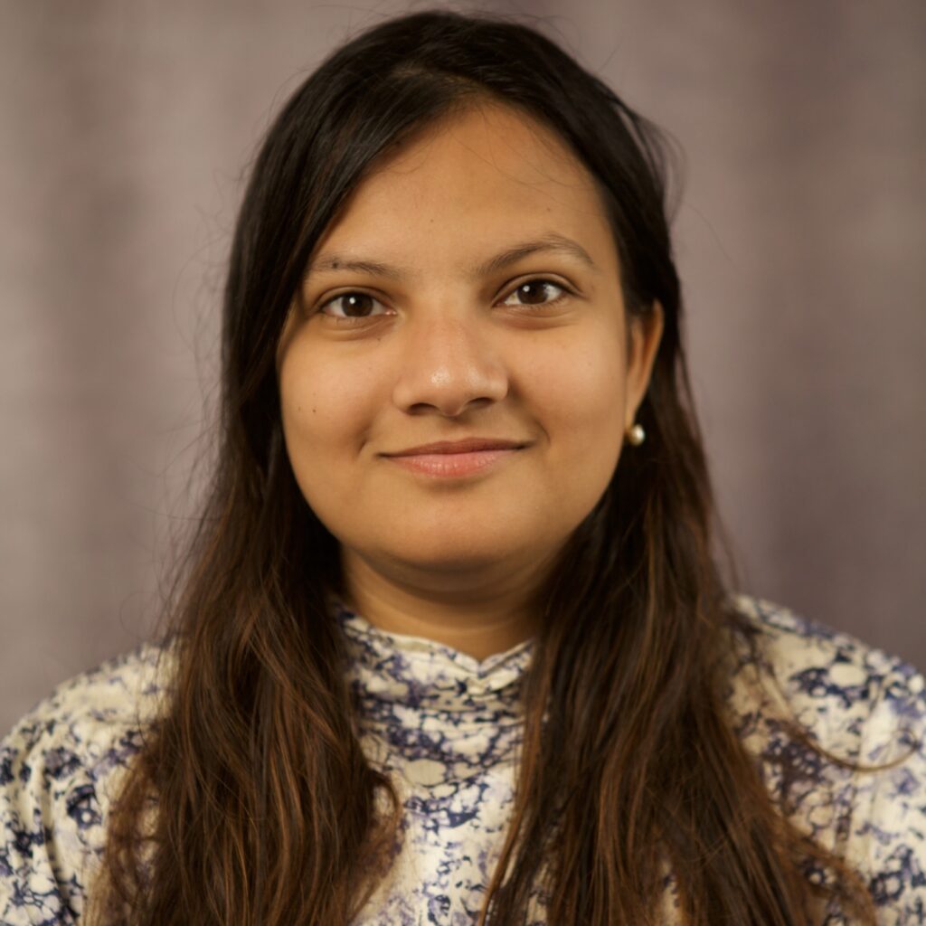 Peya Mowar, wearing a multi-color shirt in front of a grey background